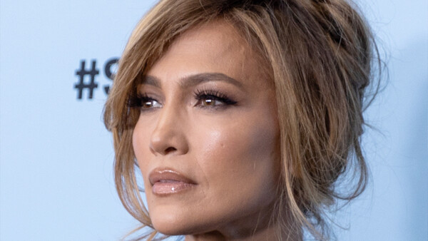 Woman's face in profile against a light blue background, showcasing soft portrait lighting and makeup.