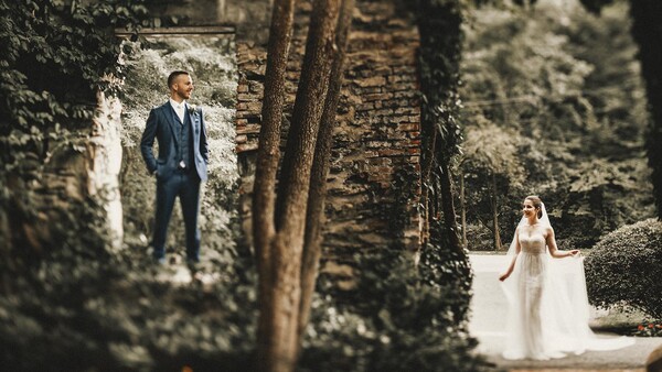 Bride and groom posed separately in an ivy-covered stone passage, bride in foreground wearing flowing white gown.