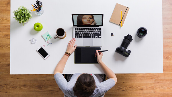 Overhead view of a photographer's workspace with laptop, camera equipment, and creative tools arranged on a white desk.