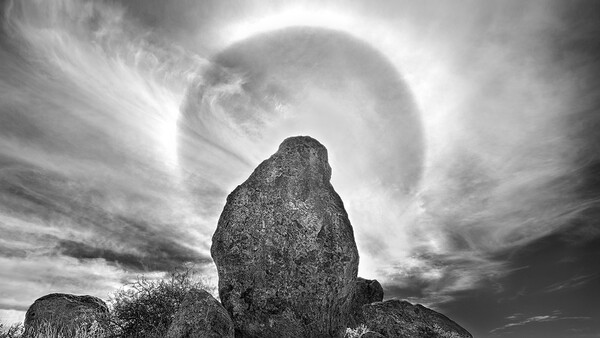 Large granite boulder silhouetted against a bright sun halo in dramatic black and white landscape.