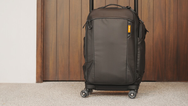 Dark gray rolling carry-on suitcase with spinner wheels against a wooden door and beige carpet.