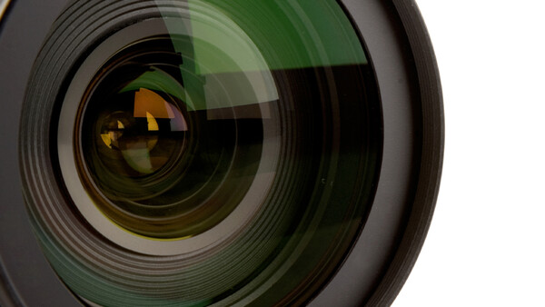 Close-up of a wide-angle camera lens with green coatings and golden reflections in the front element.
