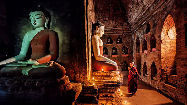 Buddhist statue illuminated in green light inside a candlelit temple chamber with brick walls.