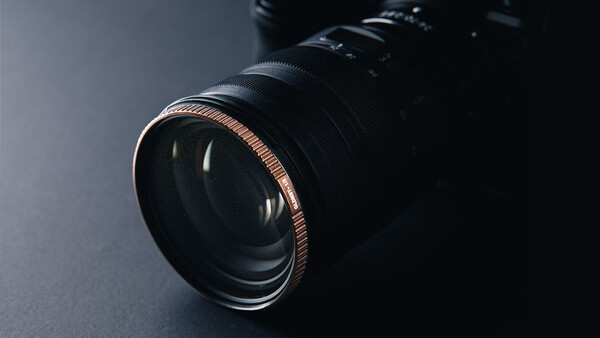 Close-up of a vintage camera lens with copper-colored focusing ring against dark background.