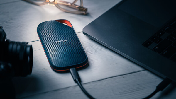 SanDisk portable external hard drive connected to laptop on white desk workspace.