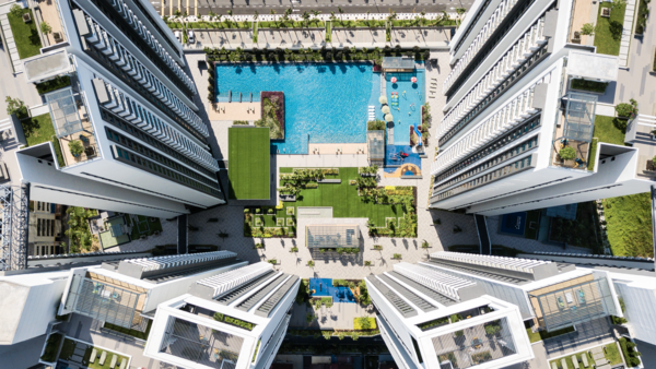 Aerial view of a modern residential complex with a bright blue swimming pool surrounded by manicured green spaces and multi-story buildings.