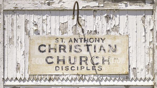 Weathered wooden sign for St. Anthony Christian Church Disciples with peeling white paint and metal frame.