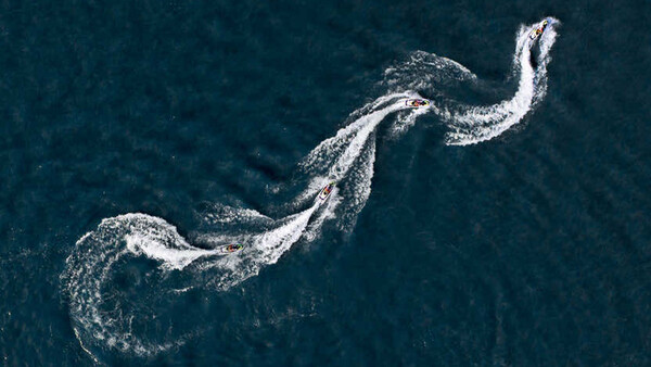 Aerial view of speedboat creating white wake patterns in dark blue ocean water.