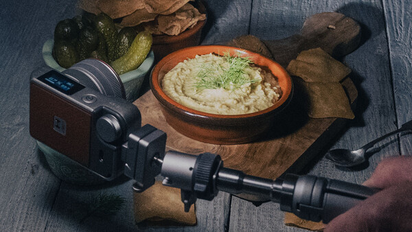 Film camera mounted on tripod with hummus and food styling setup on wooden surface.