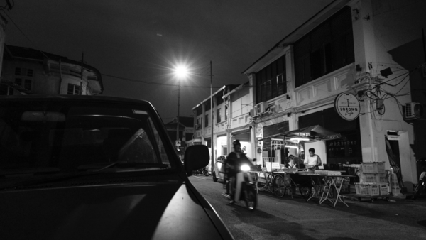 Nighttime street scene with parked truck, pedestrians, and storefronts illuminated by streetlight.