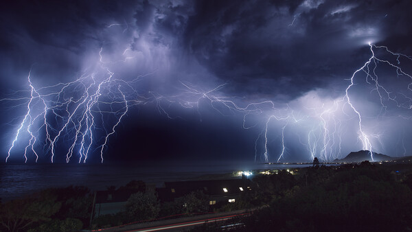 Multiple lightning bolts striking across a dark stormy sky above a distant landscape at night.