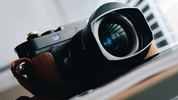 Rangefinder camera with brown leather strap and wide-angle lens, held in hand against blurred background.