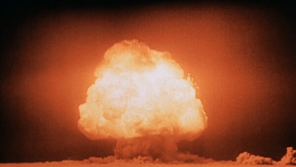 Mushroom cloud from a nuclear detonation illuminated against an orange sky at night.