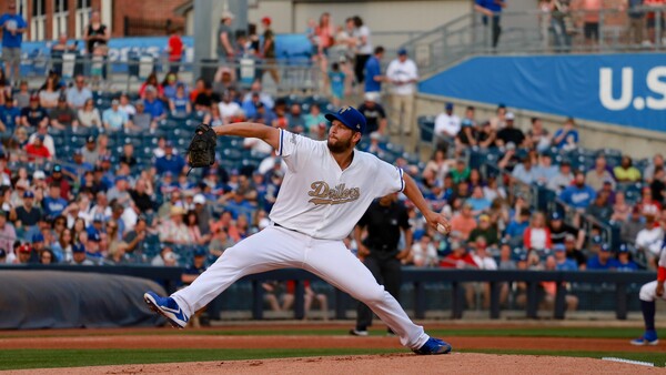 Baseball pitcher in mid-delivery, stretching across the mound in white uniform during a daytime game.