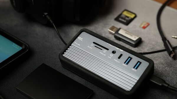 Multi-port USB hub with card reader and cables on dark desk surface.