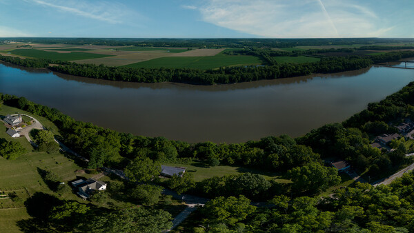 Aerial view of a meandering river with forested banks and farmland beyond.
