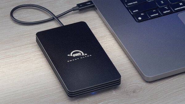 External hard drive connected via USB cable next to a laptop on a wooden desk.