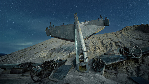 Abandoned military aircraft wreckage mounted on a desert hillside at night under starry sky.