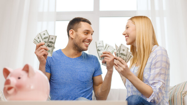 Couple holding cash and smiling at each other indoors by a window.