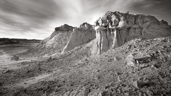 Dramatic rock formations and eroded cliffs in an arid landscape under stormy skies.