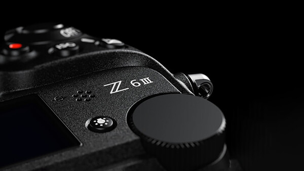 Close-up of a mirrorless camera body showing control dial and lens cap against black background.