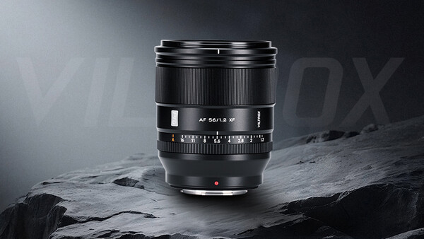 Black camera lens with manual focus ring and depth-of-field scale mounted on rocky surface.