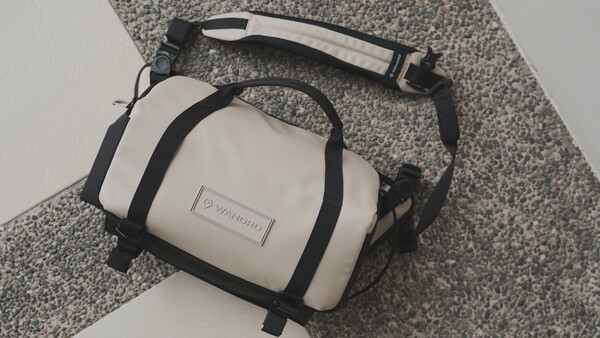 White and black compact camera bag with shoulder strap on gray textured fabric.