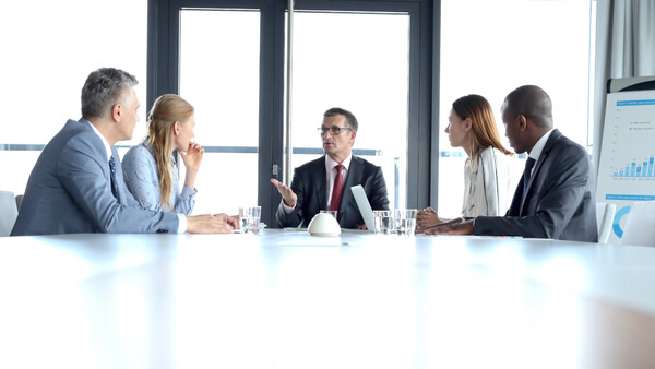 Five business professionals seated at a conference table during a meeting.