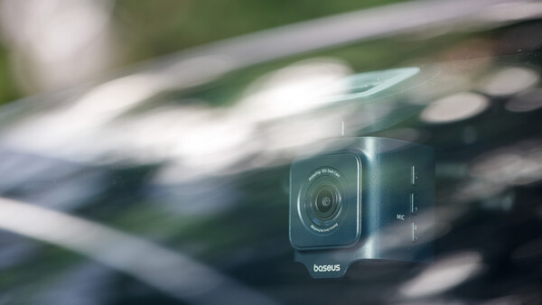 Closeup of a dash cam mounted on a vehicle windshield with blurred road ahead.