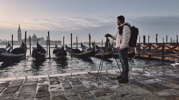 Photographer with tripod overlooking Venetian gondolas and historic architecture at dawn.
