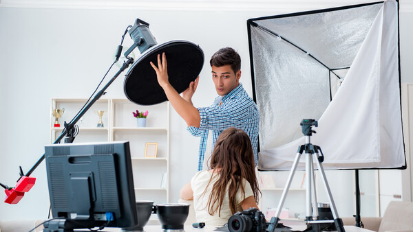 Two people adjusting a large softbox light modifier in a home photography studio setup.