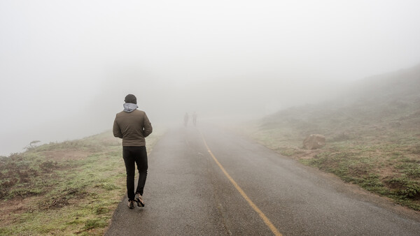 Runner jogging solo on a misty mountain road with yellow center line.