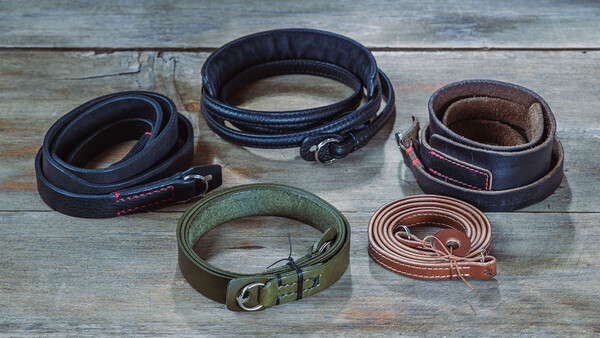 Five leather camera straps in different colors and styles arranged on weathered wood.