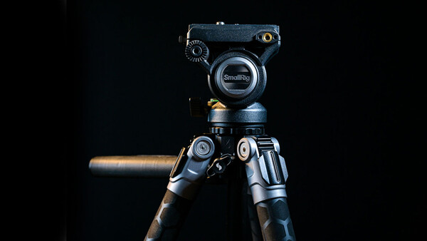 Professional video camera tripod head mounted on carbon fiber legs against a black background.