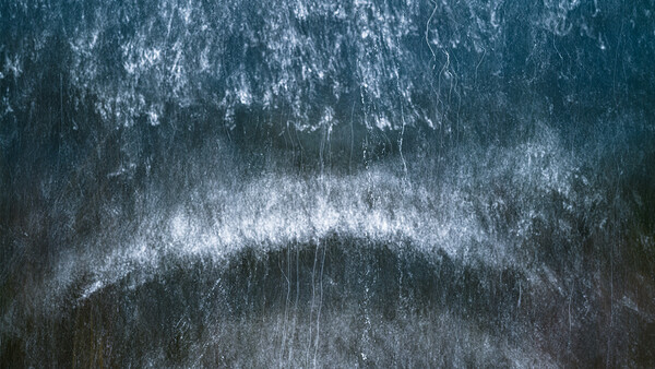 Aerial view of a snow-covered forest with a winding river cutting through dense evergreen trees.
