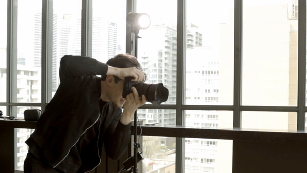 Photographer shooting with a telephoto lens from a high-rise window overlooking a city skyline.