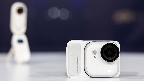 White compact camera with articulating lens and rectangular design, shown against dark background.