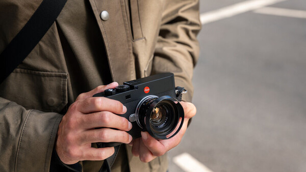 Photographer holding a rangefinder camera with a bright lens element visible in daylight.