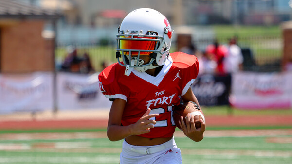 Young football player in red jersey running with the ball during a daytime game.