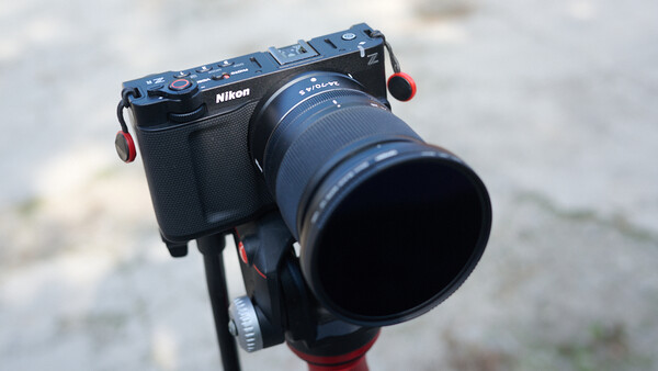 Nikon rangefinder camera with telephoto lens mounted on a red gimbal head tripod.
