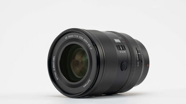 Black telephoto zoom lens with visible focus ring and distance scale on neutral background.