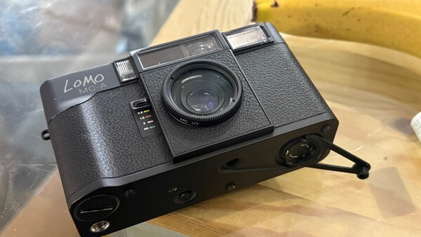 Lomo compact film camera with textured black body and manual controls positioned on wooden surface.