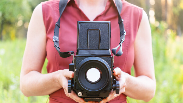 Photographer holding a medium format camera with flip-up viewfinder against their body.