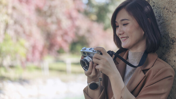 Woman holding a vintage film camera, smiling while composing a shot in soft natural light.