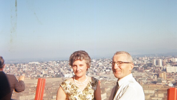 Two people standing on an elevated observation deck overlooking a sprawling cityscape at dusk.