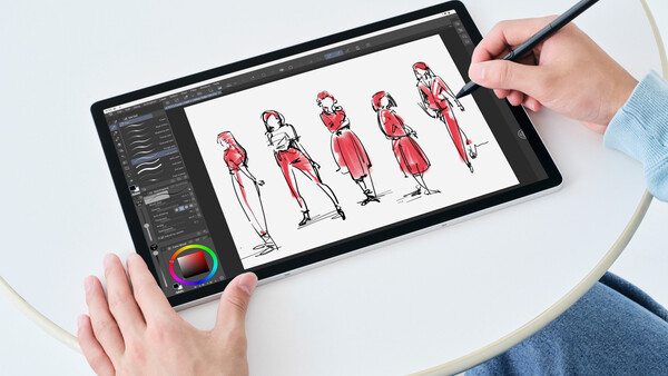 Designer using stylus on tablet displaying fashion figure sketches in red.