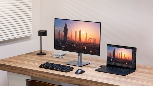 Minimalist desk setup with desktop monitor displaying cityscape at sunset and laptop positioned to the right.