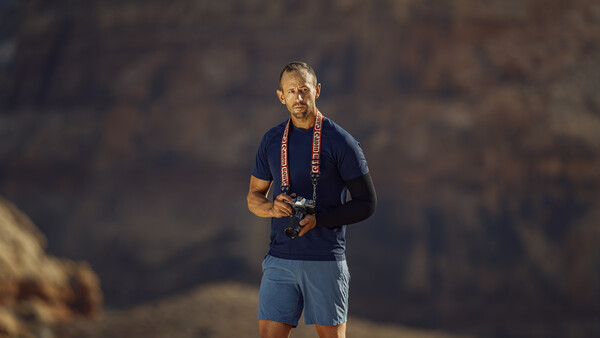 Male runner jogging outdoors at dusk wearing navy shirt, blue shorts, and a medal around his neck.
