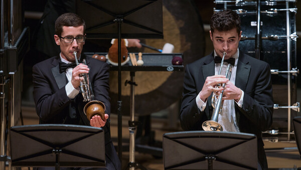 Two musicians in formal attire playing trumpets during a performance on stage.