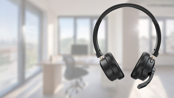Black over-ear headphones suspended against a blurred modern office interior with windows and furniture.